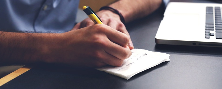 A person writing on a piece of paper with a pencil.